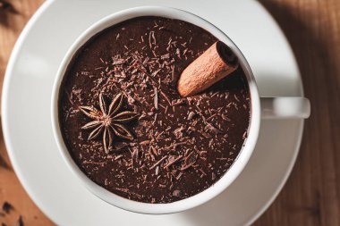 Beyaz bardakta sıcak çikolata, tarçın çubuğu ve ahşap bir masada yıldız anason..