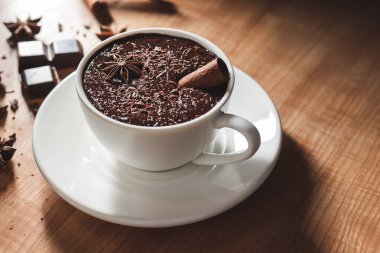 Beyaz bardakta sıcak çikolata, kırık çikolata, tarçın çubuğu ve ahşap masada yıldız anason..