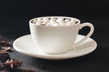 Beyaz bardakta sıcak çikolata, marşmelov, kırık çikolata küpleri ve siyah arka planda yıldız anason..