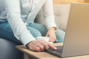 Tanınmayan bir adam, iş adamı ya da serbest çalışan biri kanepeye oturmuş, elinde kahve fincanıyla dizüstü bilgisayarda çalışıyor, evden çalışıyor..