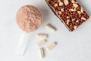 Bir kepçe süt veya soya proteini izolasyonu, çikolata protein barı, beyaz amino asit ve kreatin kapsülleri, beyaz arka planda vücut geliştiren gıda takviyeleri, üst görünüm, düz yatış.