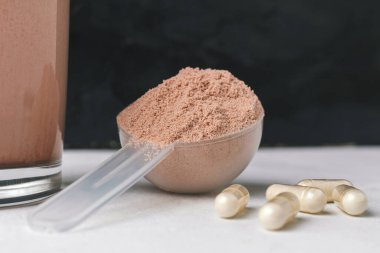 Süt ya da soya proteini kepçesi, beyaz amino asit ve kreatin kapsülleri, beyaz masa üzerinde vücut geliştirme gıda takviyeleri ve fotokopi alanı ile koyu arkaplan.