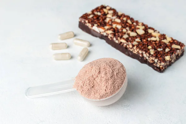 Scoop of whey or soy protein isolate, chocolate protein bar, white capsules of amino acids and creatine, bodybuilding food supplements on white background.