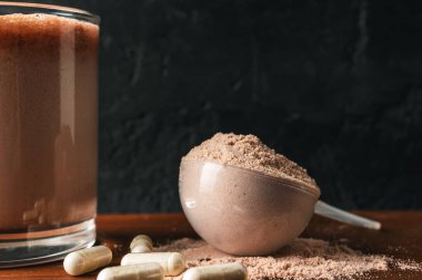 Sütlü süt tozu, kepçedeki protein tozu, beyaz amino asit ve kreatin kapsülleri, ahşap masa ve koyu arkaplanda vücut geliştirme gıda takviyeleri..