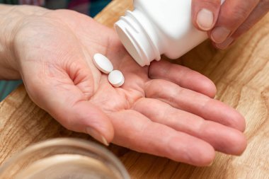 Yaşlı kadın avuç içi, ilaçlar ve vitamin takviyeleri konseptinde tedavi için beyaz ağrı kesici ya da antibiyotik hapları..