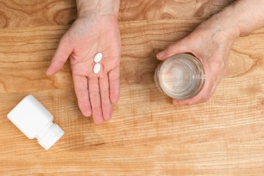 Yaşlı kadın avuçlarında tedavi için beyaz ağrı kesici ya da antibiyotik, su dolu bardak, ilaç ve vitamin takviyesi konsepti, fotokopi alanı olan üst görünüm..