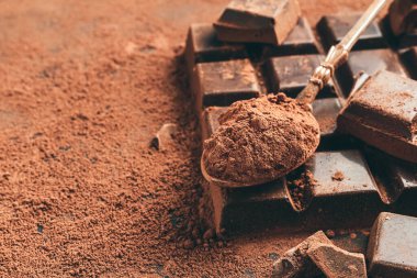 Koyu arkaplanda kahverengi kakao tozu ve doğranmış çikolata küpleri..