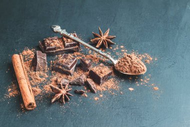 Kaşıkta kahverengi kakao tozu, çikolata küpleri, tarçın çubuğu ve fotokopi alanı olan koyu arkaplanda yıldız anason..