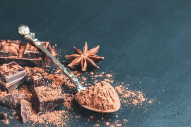 Kaşıkta kahverengi kakao tozu, çikolata küpleri ve arka planda fotokopi alanı olan yıldız anason..