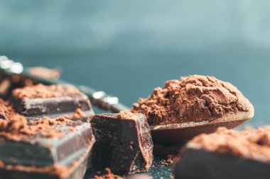 Kaşık içinde kahverengi kakao tozu ve arka planda çikolata küpleri fotokopi alanı ile..