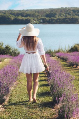 Arkadan güzel bir kızın portresi, yazın açık havada, lavanta tarlasında şapkalı çekici bir kadın..
