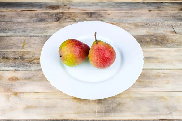 Two ripe pears in white plate on rustic wooden table — Stock Photo, Image