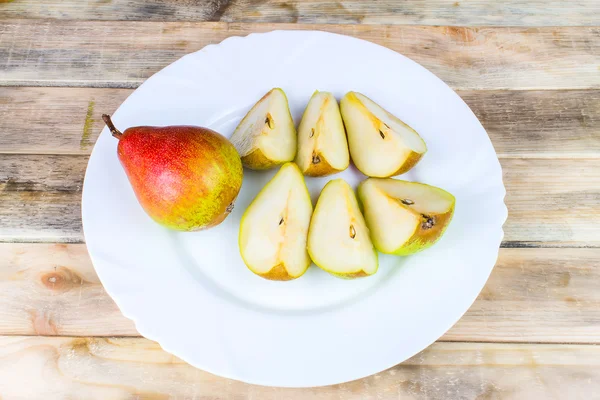 Sliced and whole pears in white plate, rustic wooden table — Stock Photo, Image