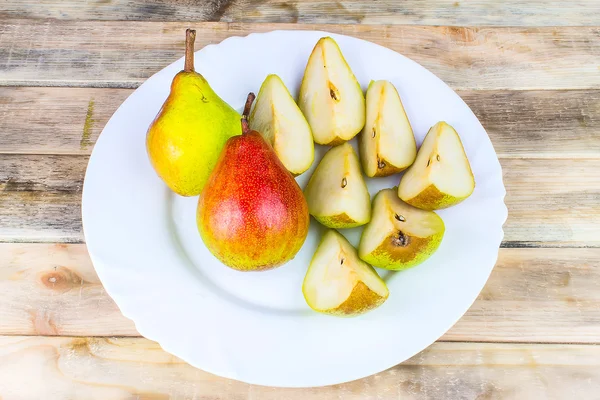 Sliced and whole pears in white plate, rustic wooden table — Stock Photo, Image