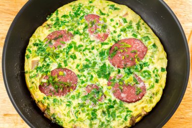 Omlete sosis ve tavada ahşap tahta üzerinde otlar ile