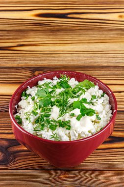 Fresh cottage cheese with sour cream, dill, parsley, onion in ceramic bowl on wooden table, space for text