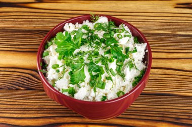 Fresh cottage cheese with sour cream, dill, parsley, onion in ceramic bowl on wooden table