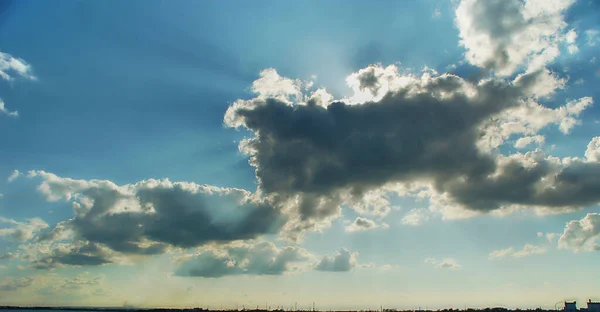 Sun behind dark clouds with sun rays on blue sky background.