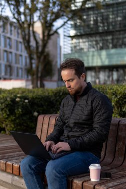 Üniversitede bankta oturan genç adam internette çalışıyor.