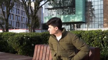 Üniversite bahçesinde oturan genç adam güneşte kahve içiyor.
