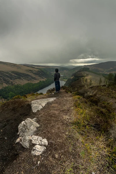 Man standing on his back on top of mountain with lake in background at Glendalough Wicklow