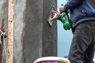 Evin ön cephesini yenilemek için duvarı sıva yapan bir adam.