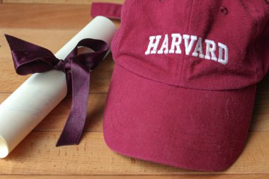 Kurdeleli mezuniyet sertifikası ve sarı ahşap arka planda bordo renginde Harvard şapkası. ABD, 2021, Nisan
