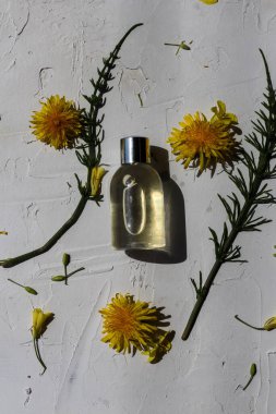 Yeşil yapraklar ve sarı çiçeklerle süslenmiş beyaz arka planda şeffaf güzellik ürünü şişesi.
