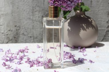 Parfüm şişesi duruyor ve etrafı leylak çiçekleriyle çevrili.