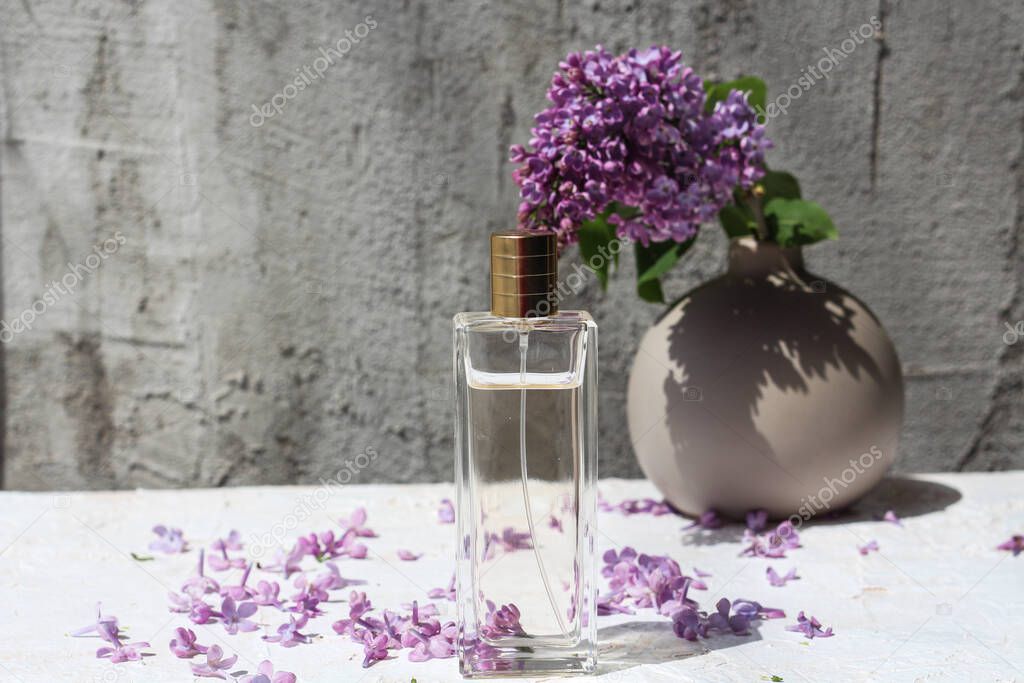 perfume bottle standing on a neutral background and surrounded by lilac flower petals