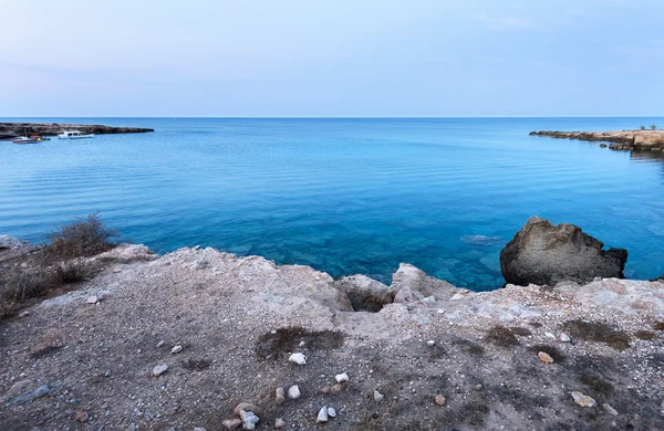 Foto av havet i protaras, Cypern ö, med stenar och båtar i solnedgången. — Stockfoto