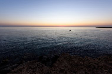 Sunrise protaras paralimni, bir balıkçı teknesi, koyu mavi deniz ve kayalar, Kıbrıs Adası suda ışığın yansıması ile