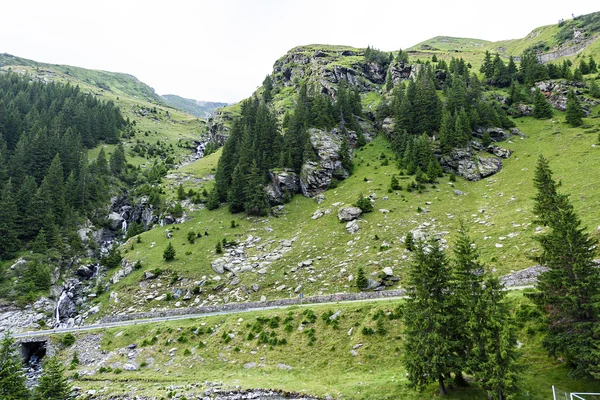 Foto de picos verdes, un pequeño río y una carretera en las montañas fagaras, Rumania . — Foto de Stock