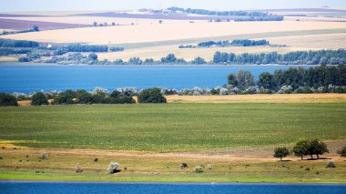 Moldova 'nın doğası, köy yolu ve yeşilliği olan çayır, ön ve arka planda göl, tarlalar ve uzaktan görülebilen ender binalar