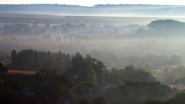 Moldova 'da güneş doğarken sislerin arasından görülebilen yerleşim evleri ve çoklu yeşilliğe sahip bir köy
