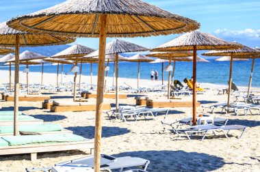 Yunanistan 'ın Asprovalta kentindeki boş plajda Reed şemsiyeleri ve güneş yatakları