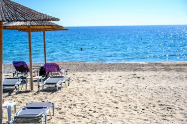 Yunanistan 'ın Asprovalta kentindeki boş plajda Reed şemsiyeleri ve güneş yatakları