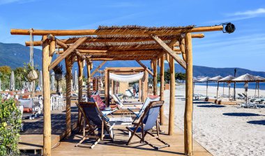 Yunanistan 'ın Asprovalta kentindeki boş plajda dinlenme masalı Reed şemsiyeleri ve güneş yatakları