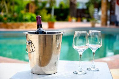 Kırmızı şarap şişesi ve otel havuzunun yanındaki bardaklar.