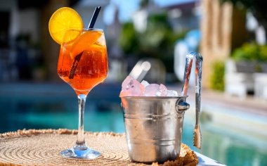 Kırmızı kokteyl, turuncu dilimli ve buzlu otel havuzunun yanında.