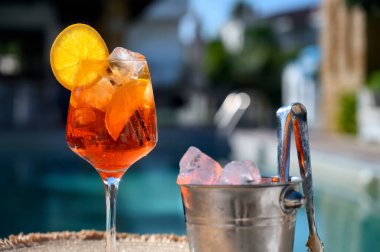 Kırmızı kokteyl, turuncu dilimli ve buzlu otel havuzunun yanında.