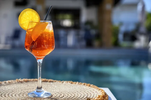 Red cocktail with orange slice and ice near a hotel pool