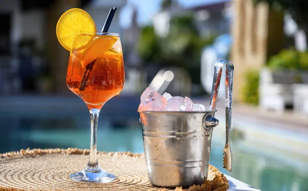 Red cocktail with orange slice and ice near a hotel pool