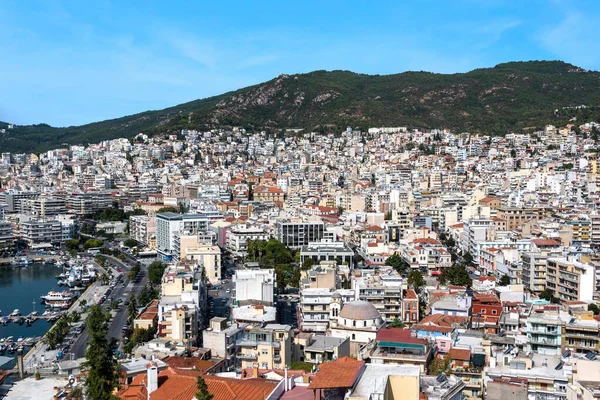 Birden fazla konut ve devlet binası, arka planda yeşil tepeler, Yunanistan 'ın Kavala kentinde demirli yatları olan Ege deniz maliyeti
