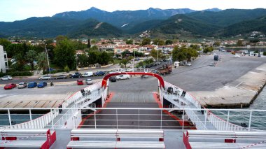 Demir atmış feribot, Thassos limanında iskele, yeşil tepeler, yol, kasaba ve park halindeki arabalar Yunanistan 'da arka planda.