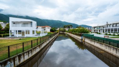 Çevresinde konut ve yeşillik bulunan su kanalı, arka planda bitki örtüsü bulunan tepe, Stavros, Yunanistan
