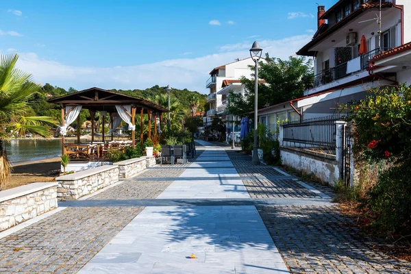 Pedestrial street on the Aegean sea shore with commercial buildings, gazebo and lush greenery in Olympiada, Greece