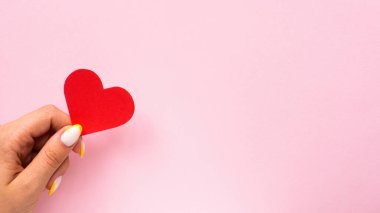 Kadın eli pembe arka planda kırmızı bir kalp tutar. Tatil konsepti. Ön görünüm