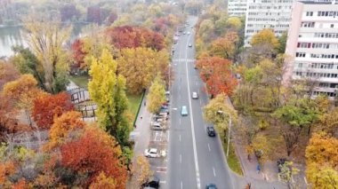 Göl kenarındaki Titan parkı ve çok renkli ağaçlar, hareket halindeki arabalarla yol ve parkın yakınındaki konut binaları. İHA, Bükreş ve Romanya 'dan görüntü