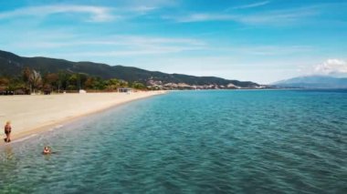 ASPROVALTA, GREECE - 25 Eylül 2020: Arkasında yeşil tepeler olan Ege deniz kıyısının panoraması. Long Beach. Dinlenen insanlar. Güneşli bir gün